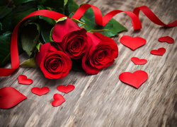 Trzy czerwone róże ze wstążką obok rozsypanych serduszek