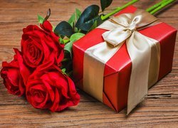 Trzy czerwone sztuczne róże obok prezentu