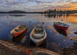 Trzy łódki zacumowane przy brzegu jeziora o wschodzie słońca