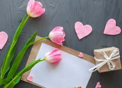 Tulipany i różowe serduszka obok kartki i prezentu