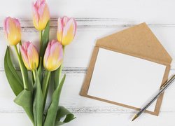 Tulipany obok kartki i długopisu na deskach