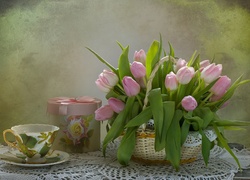 Tulipany w koszyku obok filiżanki i kolorowego pudełka na stoliku