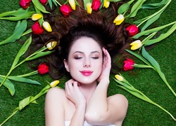 Tulipany wokół rozmarzonej kobiety leżącej na trawie