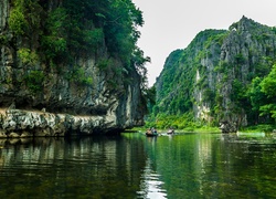 Turyści w łódach płynących po wietnamskiej rzece między skałami