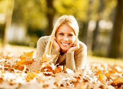 Uśmiechnięta blondynka na łące wśród jesiennych liści