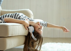 Uśmiechnięta dziewczyna ze słuchawkami na uszach leży na kanapie