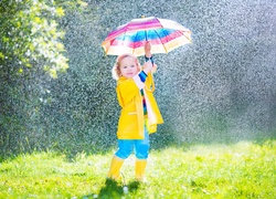 Uśmiechnięta dziewczynka pod parasolem w deszczowy dzień