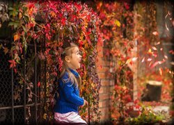 Uśmiechnięta dziewczynka przy ogrodzeniu porośniętym winobluszczem jesienną porą