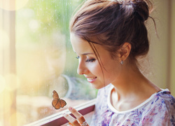 Uśmiechnięta kobieta obserwuje motyla na oknie