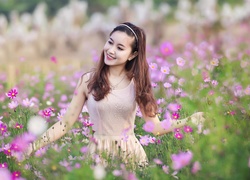 Uśmiechnięta kobieta pośród kwiatów kosmei na łące