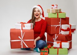Uśmiechnięta kobieta w czapce Mikołaja wśród prezentów