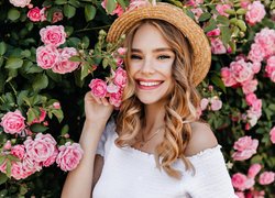 Uśmiechnięta kobieta w kapeluszu przy różanym krzewie