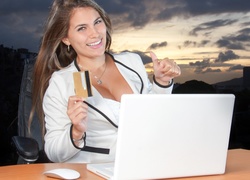 Uśmiechnięta kobieta z kartą kredytową w dłoni siedzi przed laptopem