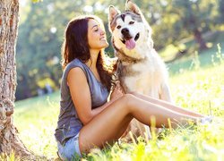 Uśmiechnięta kobieta z psem rasy siberian husky na łące pod drzewem