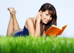 Uśmiechnięta szatynka z książką na trawie