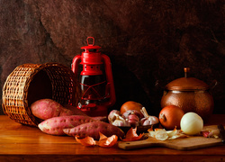 Warzywna kompozycja z batatów, cebuli i czosnku obok lampy naftowej