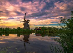 Wiatrak obok domu nad kanałem w Kinderdijk pod kolorowym niebem zachodzącego słońca