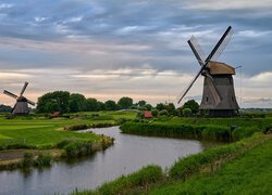 Wiatraki nad rzeką pod zachmurzonym niebem