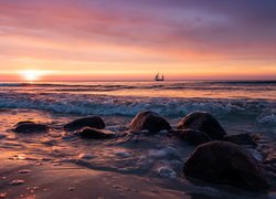 Widok z brzegu morza na żaglówkę i wschód słońca