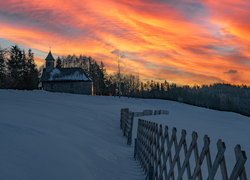 Widok z zaśnieżonej łąki na zachód słońca nad kościołem i lasem