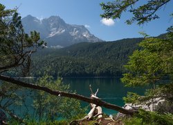 Widok znad jeziora na skaliste góry i zalesione wzgórze