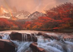 Widok znad rwącej rzeki na tęczę nad szczytem Fitz Roy