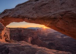 Widok zza łuku skalnego Mesa Arch na zachód słońca nad Parkiem Narodowym Canyonlands