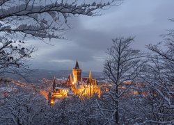 Widok zza ośnieżonych drzew na oświetlony Zamek Wernigerode