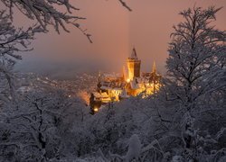 Widok zza ośnieżonych drzew na oświetlony Zamek Wernigerode