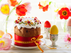 Wielkanocna babka z lukrem obok kolorowych jajek i kwiatów
