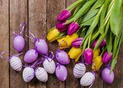 Wielkanocne pisanki z kokardkami obok kolorowych tulipanów