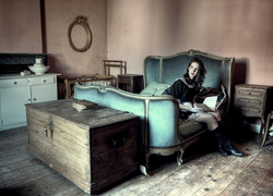Wnętrze starego mieszkania z kobietą siedzącą na łóżku i kufrem
