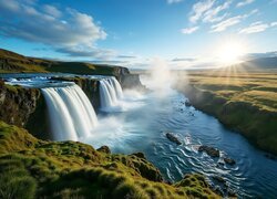 Wodospady spływające do rzeki w promieniach słońca