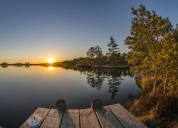 Wschodzące słońce oświetlające pomost, jezioro i otaczające je drzewa