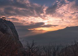 Zachodzące słońce wyzierające zza chmur nad górami