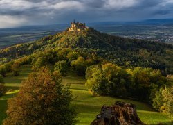 Zamek Hohenzollern na zalesionej górze pod ciemnymi chmurami