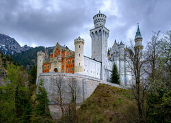 Zamek Neuschwanstein otoczony drzewami na tle Alp Bawarskich