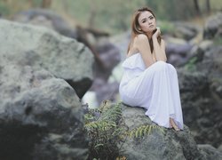 Zamyślona kobieta w białej sukience na skale
