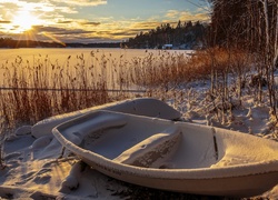 Zaśnieżona łódź nad brzegiem jeziora