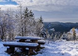 Zaśnieżone drewniane ławki ze stolikiem w plenerze z widokiem na góry