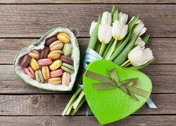 Zielone pudełko w kształcie serca z makaronikami obok białych tulipanów na deskach