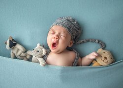 Ziewające niemowlę wśród pluszowych zabawek