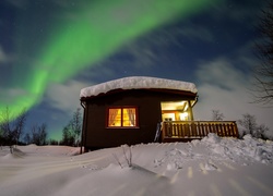 Zorza polarna nad oświetlonym domem w pobliżu lasu