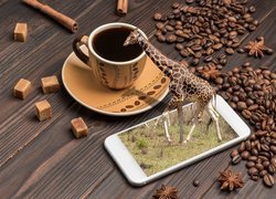 Żyrafa wychodząca z telefonu obok filiżanki kawy